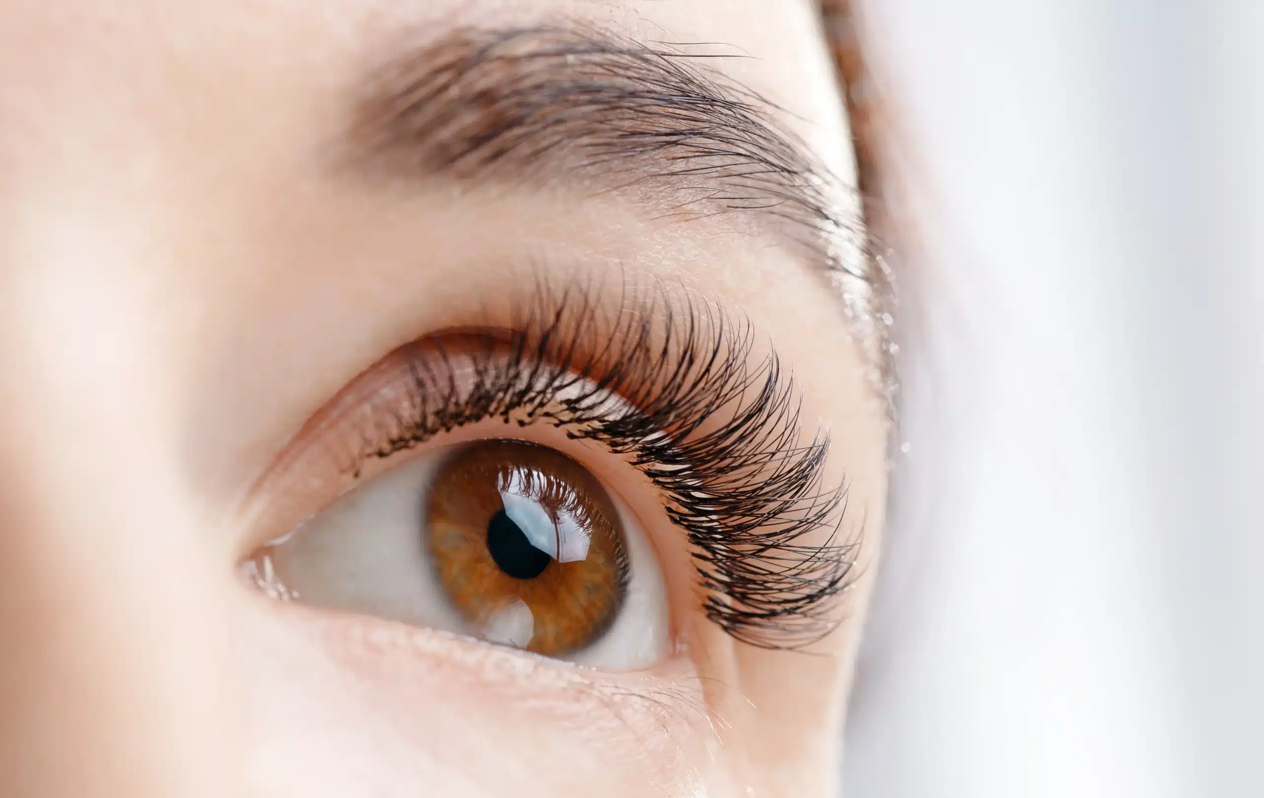 Gros plan d'un œil brun avec des extensions de cils noires, volumineuses et recourbées pour un regard intense.