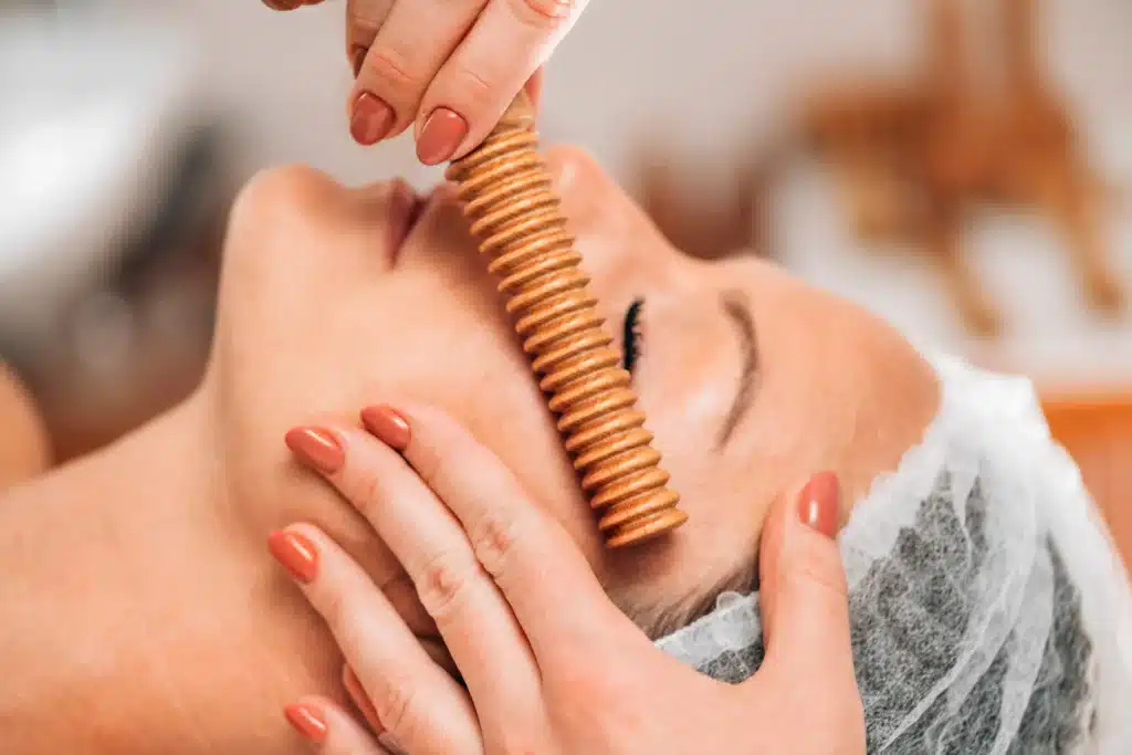 Madérothérapie Visage : Massage au Rouleau en Bois Massage facial à la madérothérapie avec un rouleau en bois strié pour un soin du visage relaxant et drainant.